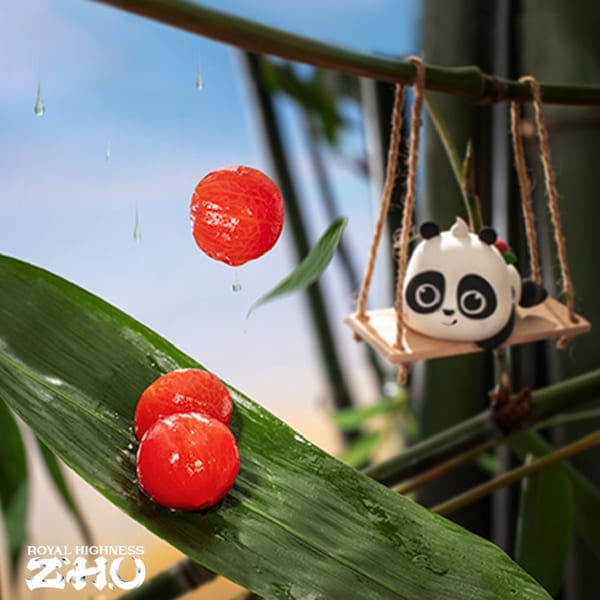 A panda-shaped dessert on a swing, with red berries and bamboo leaves, against a blue sky.
